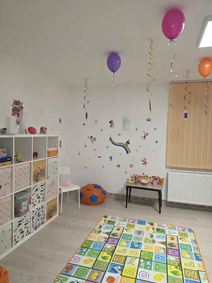 Sala de joacă cu covor educativ cu litere și cifre, rafturi cu jucării și baloane la inaugurarea Harmony Club School