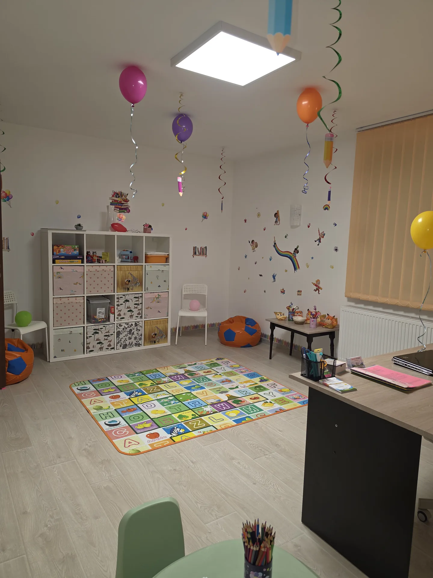 Sala de joacă decorată cu baloane colorate, covor educativ și fotolii puf pentru copii