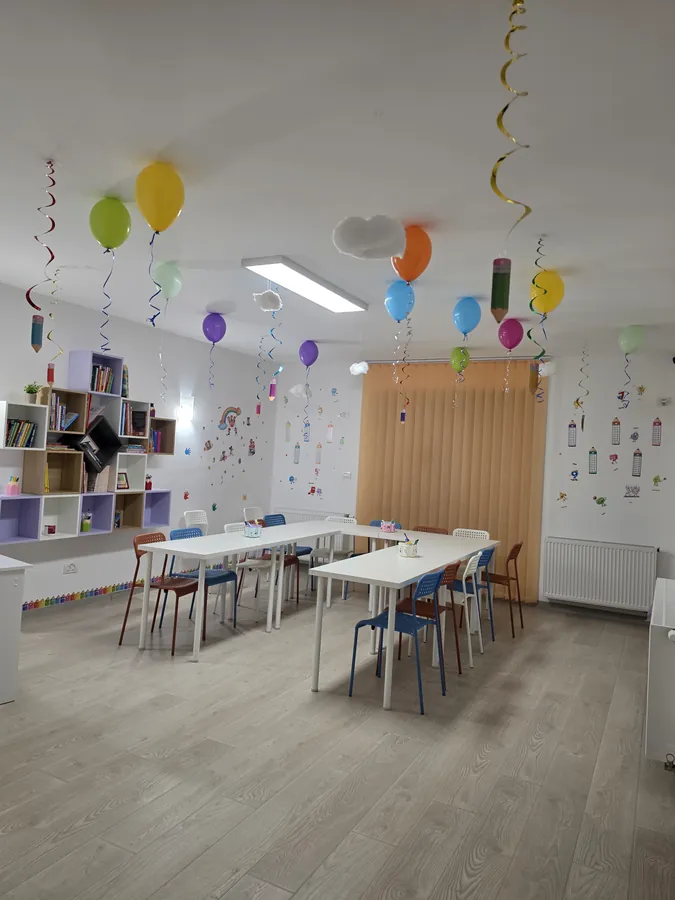 Sala de clasă cu mese de lucru, bibliotecă și perete decorat cu autocolante vesele