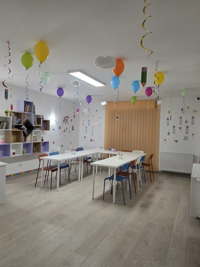 Sala de clasă aranjată pe rânduri, cu raft de cărți și lumină naturală