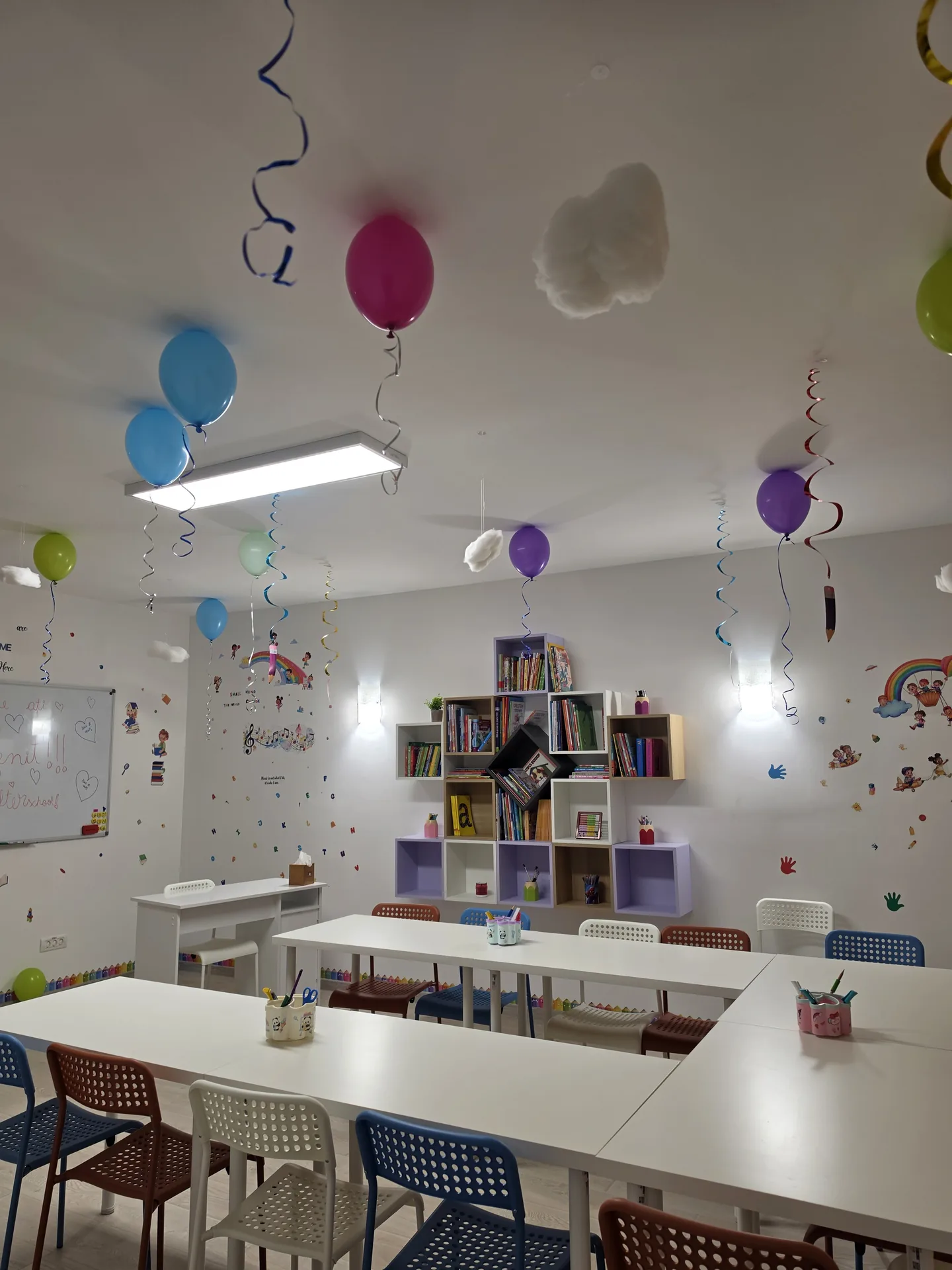 Sala de clasă cu mesele așezate în formă de U, tablă albă și colț de lectură