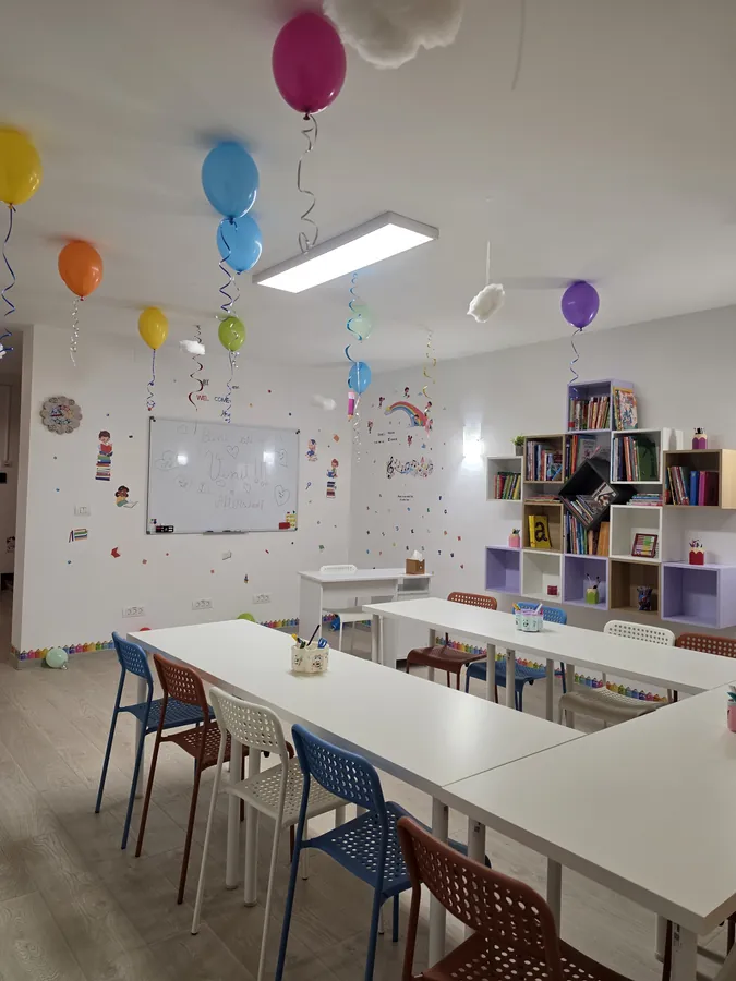 Sala de clasă cu tablă albă, bibliotecă și scaune colorate pentru copii