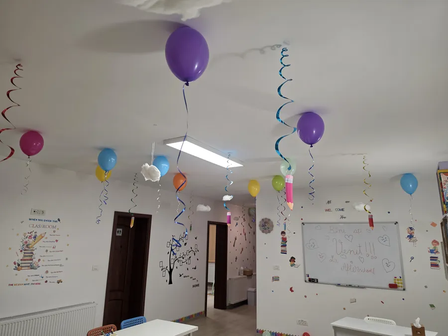 Sala de clasă văzută dinspre intrare, cu tablă albă și decor cu baloane