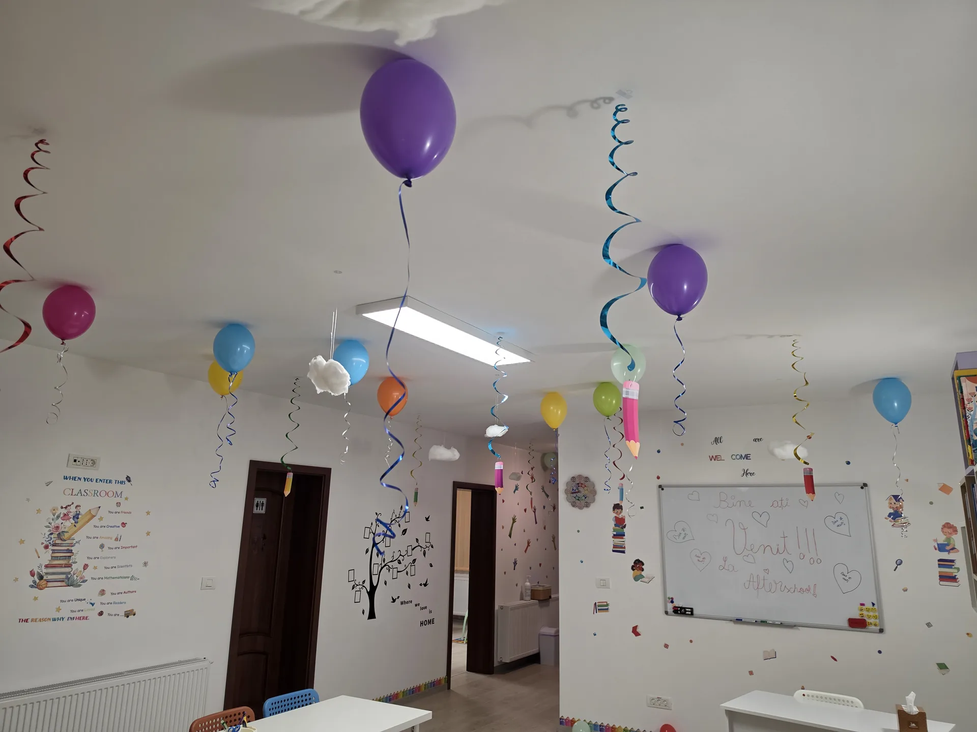 Sala de clasă văzută dinspre intrare, cu tablă albă și decor cu baloane