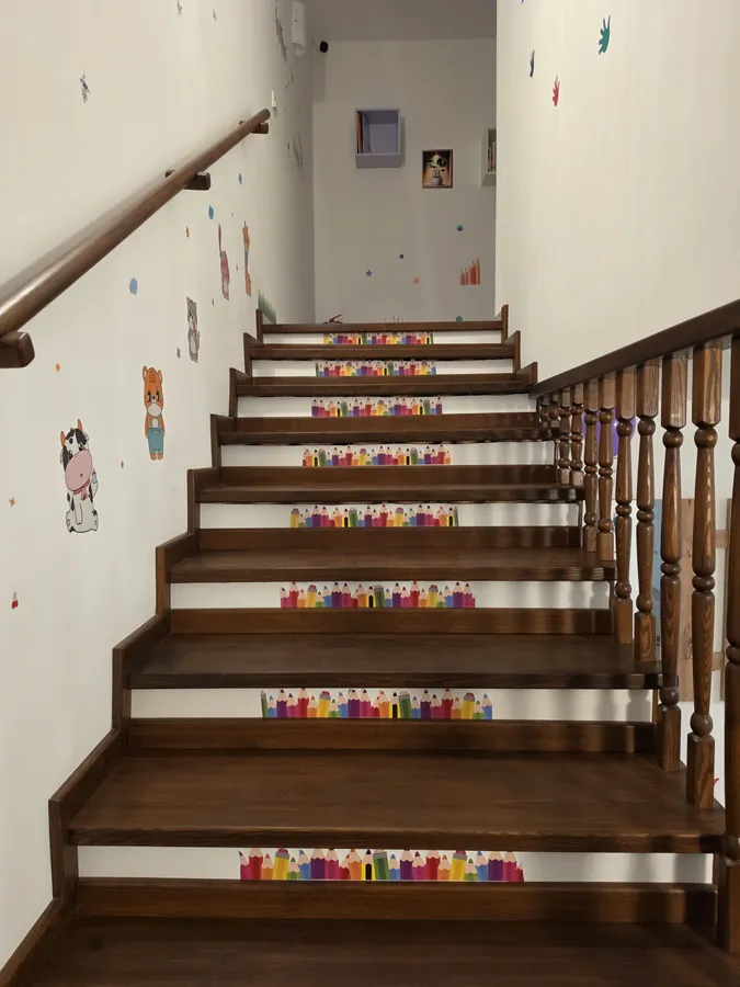Scara către etaj, cu balustradă din lemn și decorațiuni vesele pe trepte
