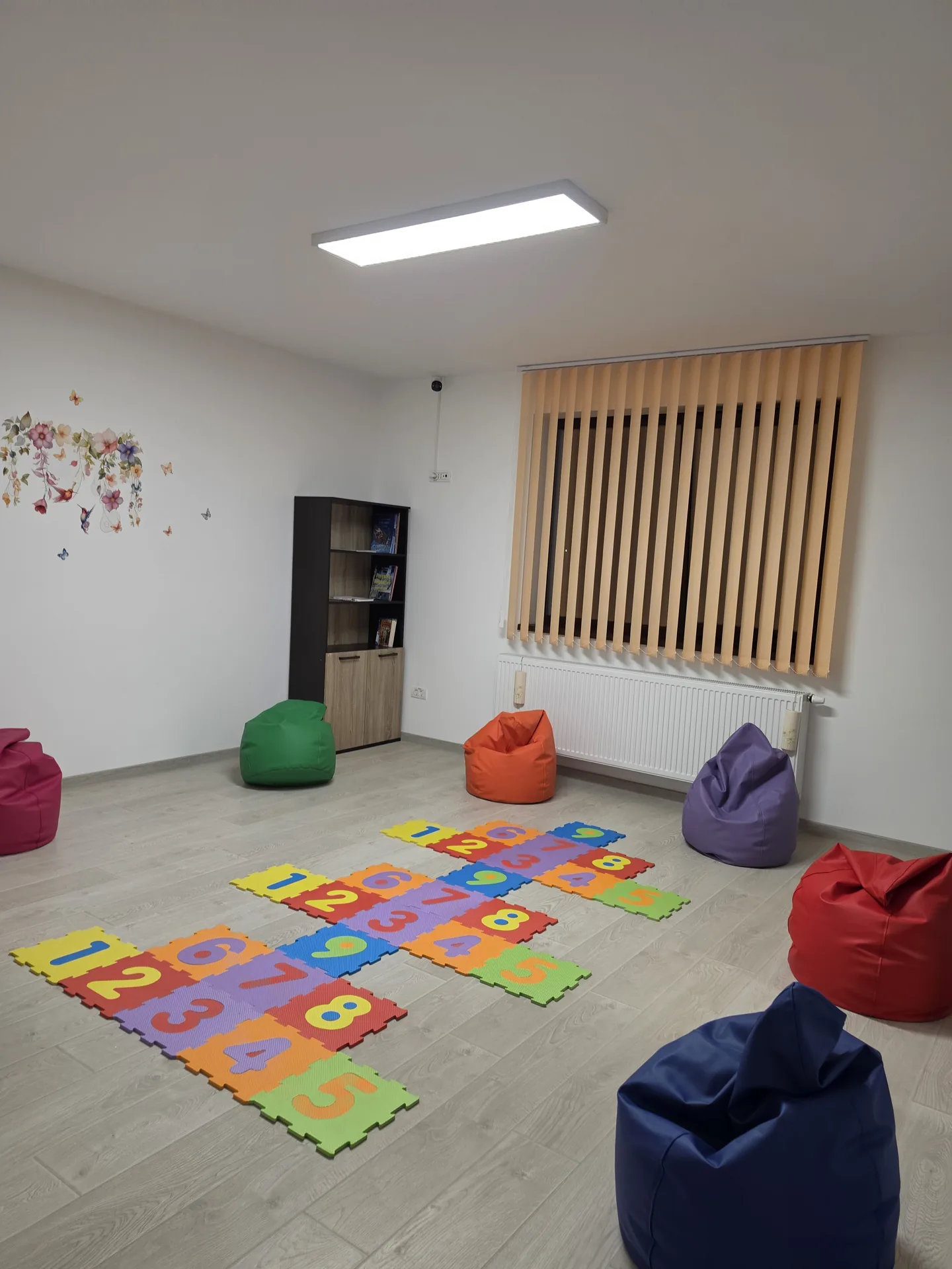 Sala de joacă cu puzzle cu cifre, fotolii puf colorate și bibliotecă